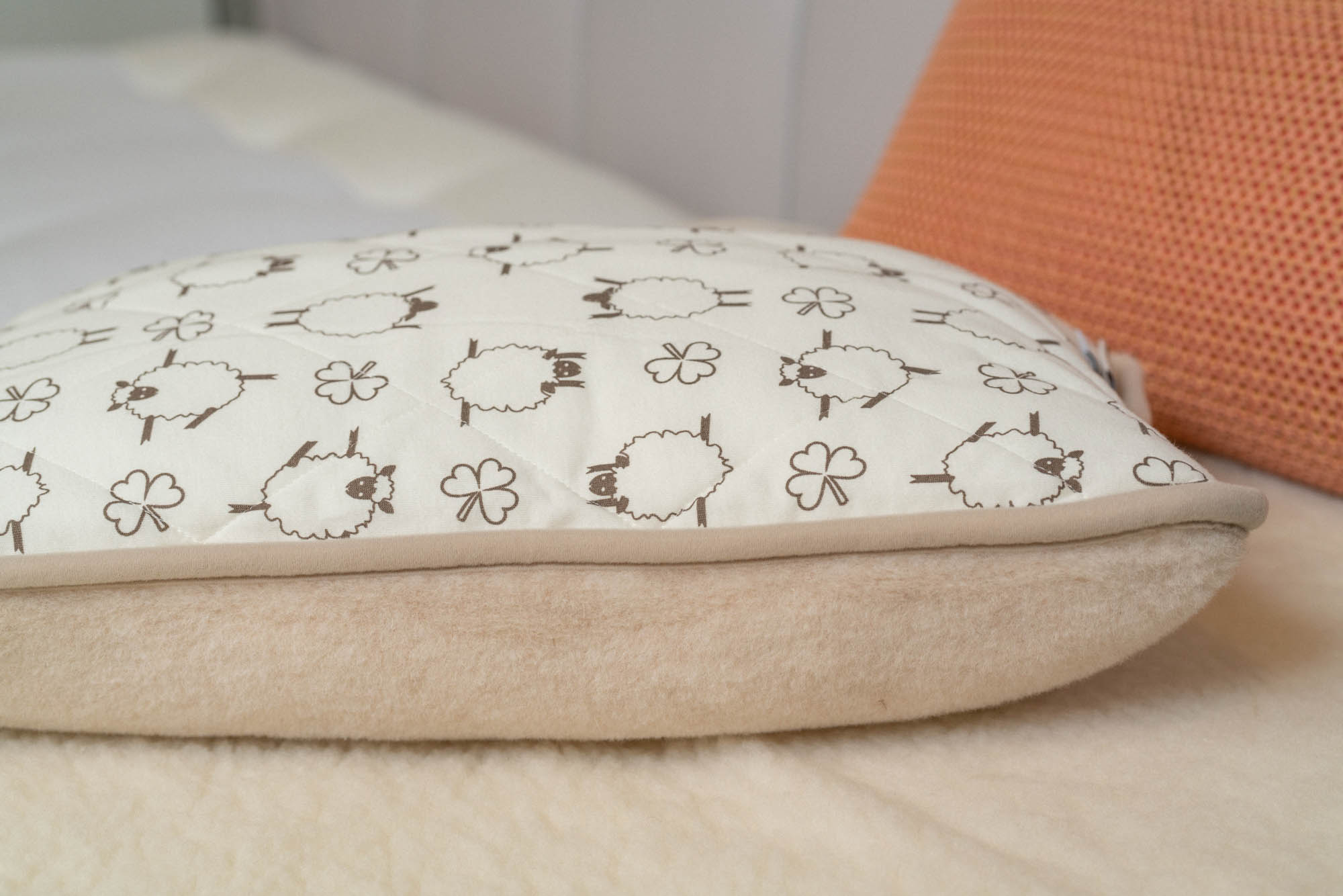 Seitenansicht des Flokati Moka Kinderkissen in beige mit Schaf- und Kleeblattmuster